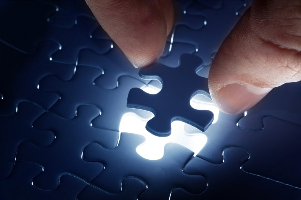 Person putting a blue puzzle piece into a puzzle. The puzzle is backlit.